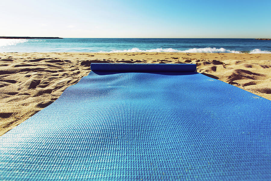 Blue yoga mat is on a sandy beach by the sea. Barcelona, Spain by Anna  Finist