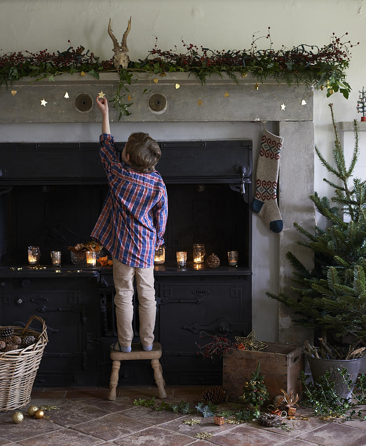 Boy decorating Christmas fireplace #1 Photograph by Paul Viant