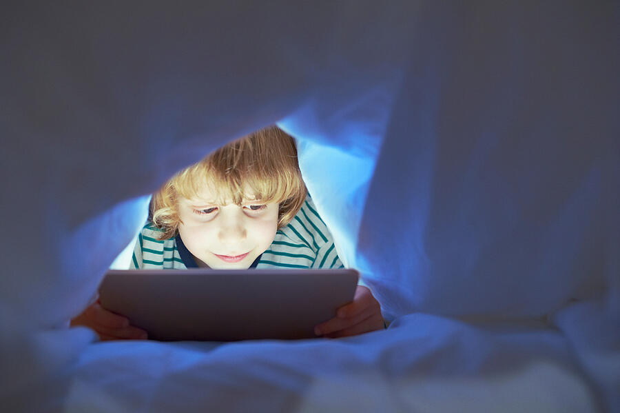 Boy underneath duvet using digital tablet #1 Photograph by Adrian Weinbrecht