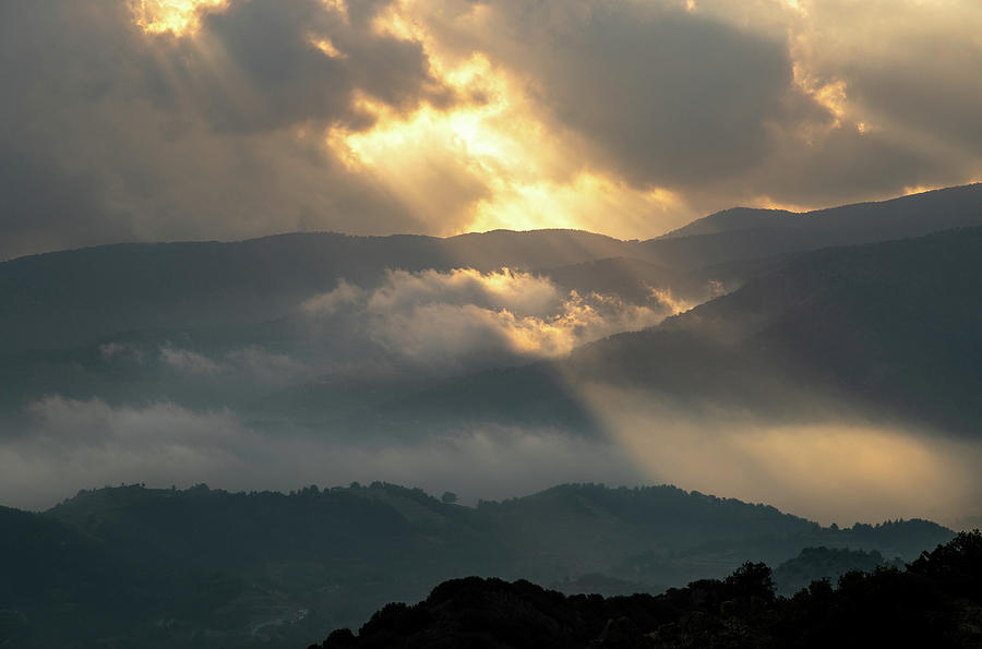Bright sun rays light shining through dark clouds over mountain at sunset. Dramatic sky in winter #1 Photograph by Michalakis Ppalis