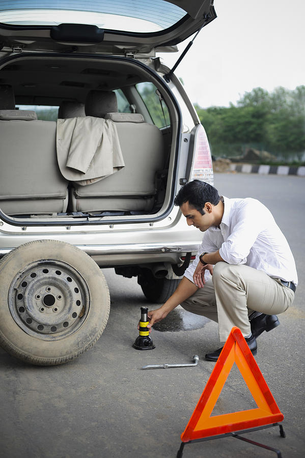 Businessman changing a car tire at roadside #1 Photograph by Uniquely India