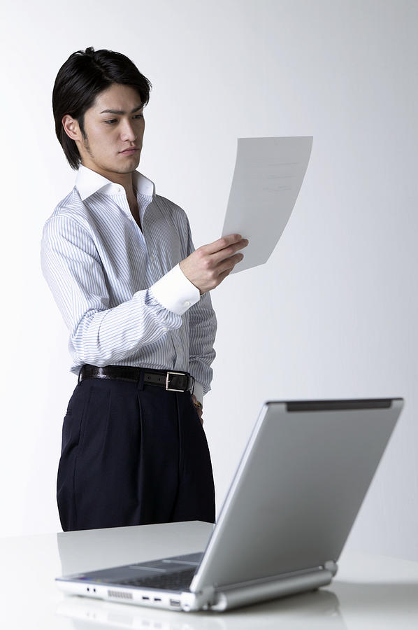 Businessman Looking at a Document With a Laptop in the Foreground #1 Photograph by Mash