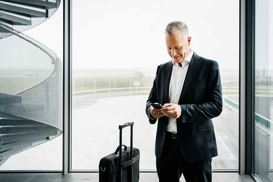 Businessman with smart phone standing at airport #1 Photograph by Hinterhaus Productions