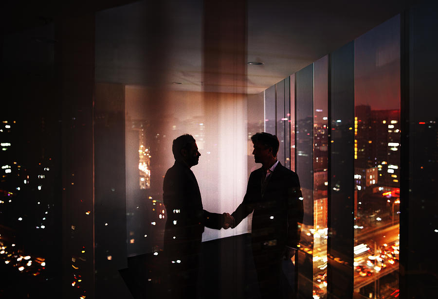 Businessmen shaking hands in office at night with city view #1 Photograph by FangXiaNuo