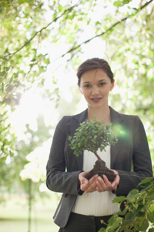 Businesswoman standing outdoors holding plant #1 Photograph by Paul Bradbury