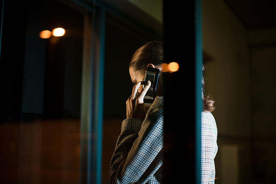 Businesswoman using mobile phone in office at night #1 Photograph by Image Source