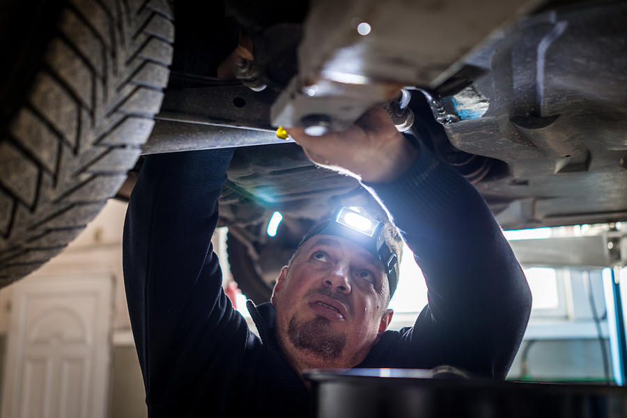Car mechanic working under a vehicle at workshop #1 Photograph by Jasmin Merdan