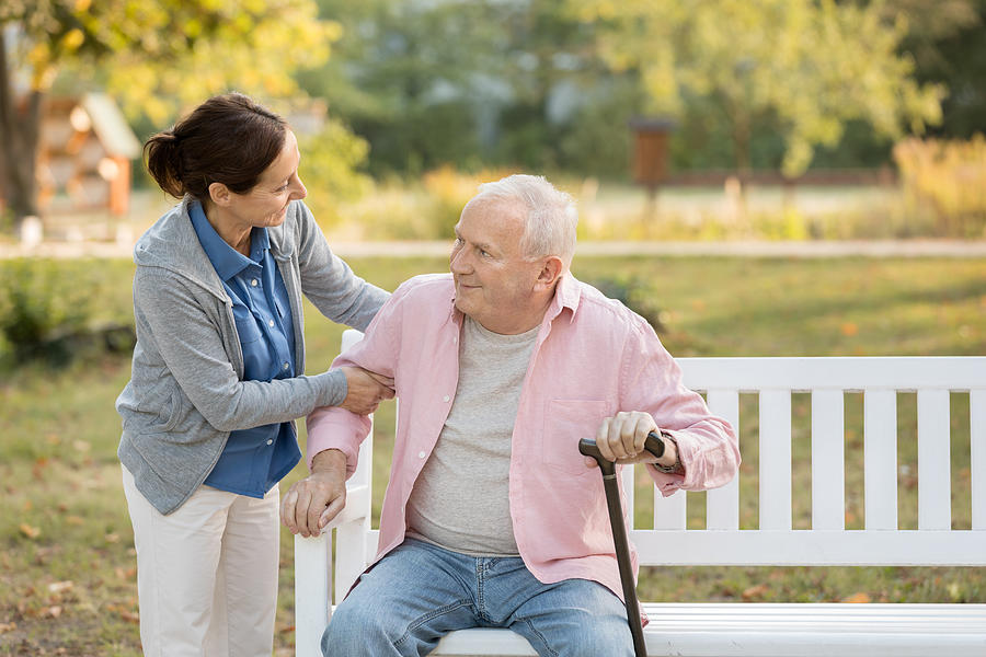 Caregiver and senior man in the park on park bench #1 Photograph by FredFroese