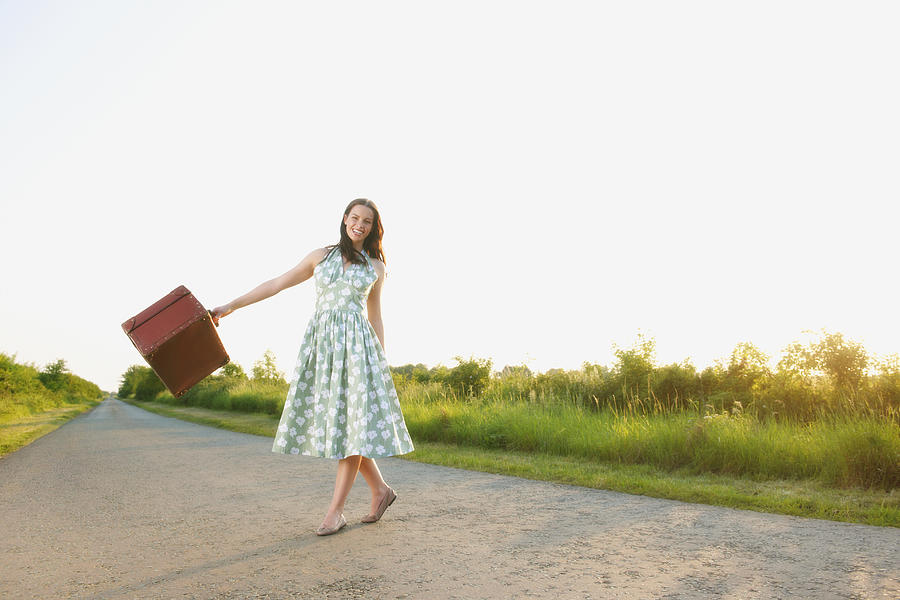 Caucasian woman carrying suitcase on rural road #1 Photograph by Jacobs Stock Photography Ltd