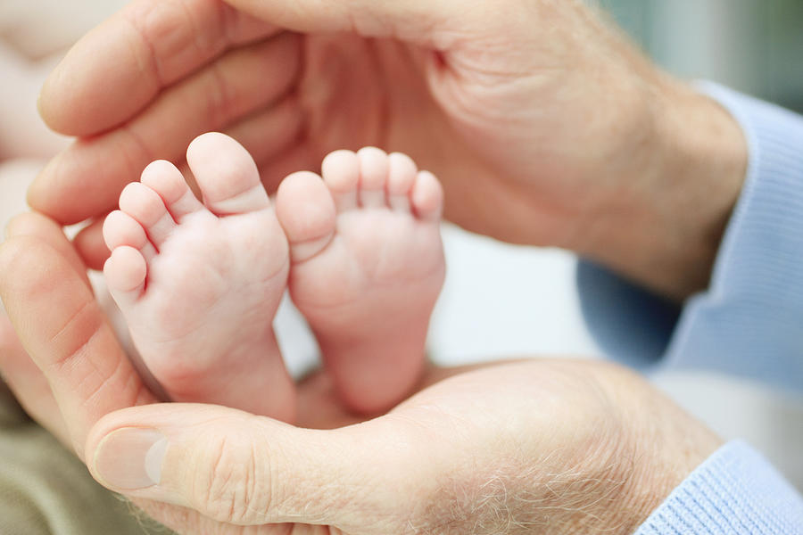 Close up of babys feet in grandfathers hands #1 Photograph by Tom Merton