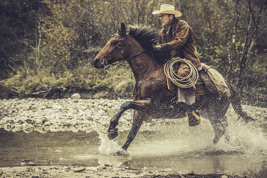 Cowboy riding across a river in the forest #1 Photograph by Vm