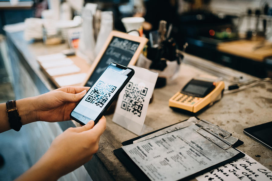 Customer scanning QR code, making a quick and easy contactless payment with her smartphone in a cafe #1 Photograph by AsiaVision