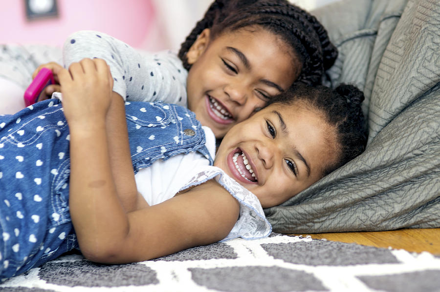 Cute African American girl tickling younger sister on the floor #1 Photograph by FatCamera