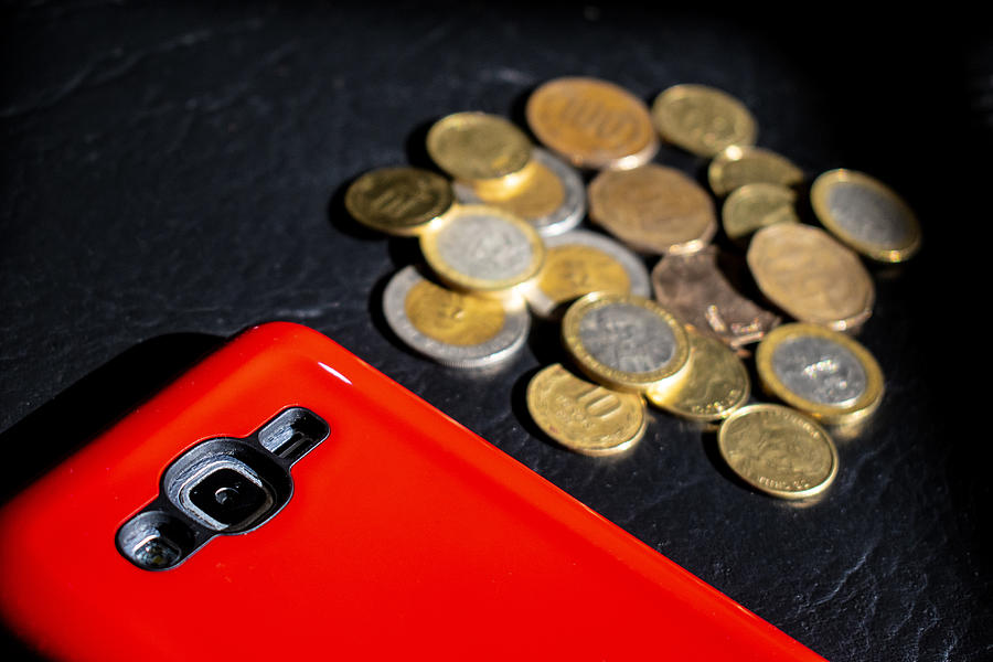 Dinero en efectivo: pesos chilenos en monedas y teléfono celular/móvil con protector rojo #1 Photograph by Javier Ghersi