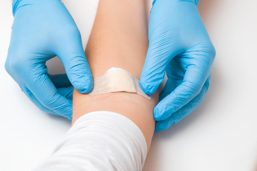 Doctor in blue rubber protective gloves putting an adhesive bandage on young womans arm vein after blood test or injection of vaccine. First aid. Medical, pharmacy and healthcare concept. Closeup. #1 Photograph by FotoDuets