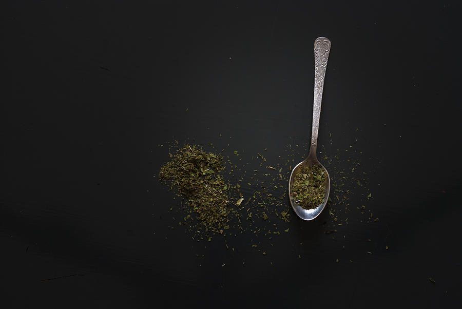 Dried basil on metal teaspoon on dark wooden table #1 Photograph by MichalDziedziak