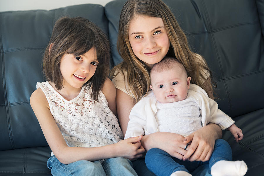 Family portrait of three sisters sitting on couch at home. #1 Photograph by Martinedoucet