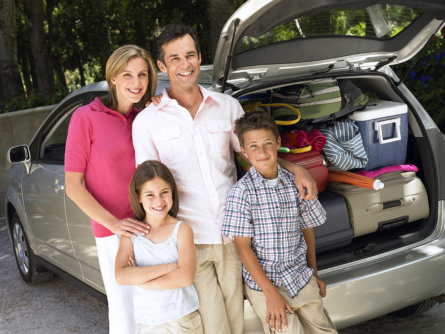 Family standing by car loaded with cases, smiling, portrait #1 Photograph by Flying Colours Ltd