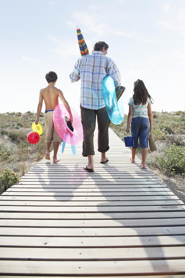 Father and children (7-9) on path carrying beach toys, rear view #1 Photograph by Getty Images