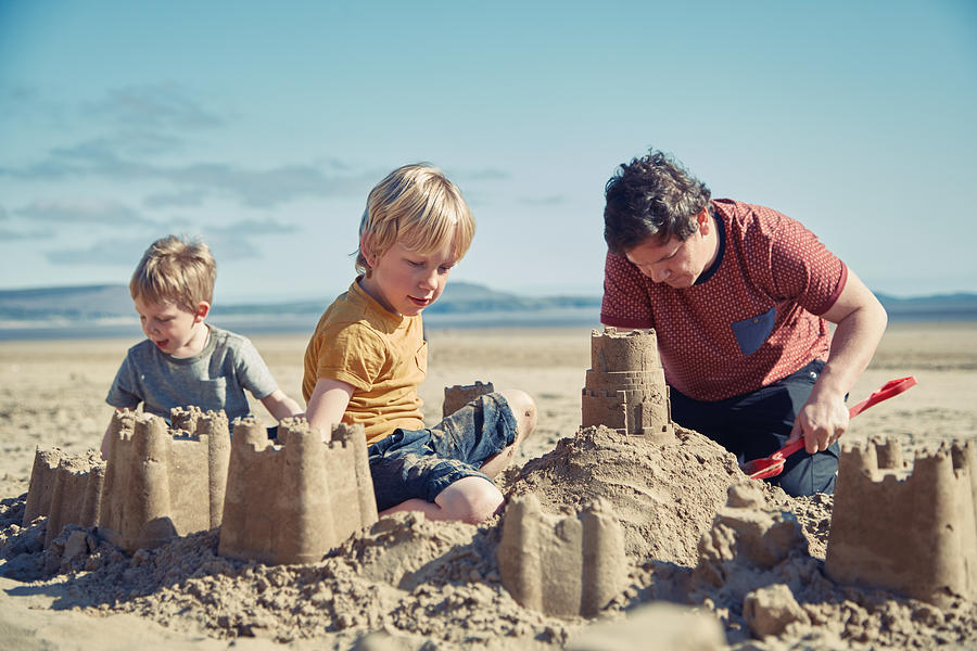 Father and sons playing on the beach #1 Photograph by Sally Anscombe