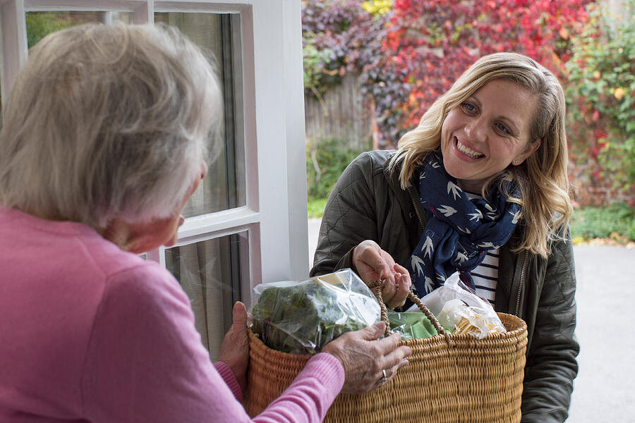 Female Neighbor Helping Senior Woman With Shopping #1 Photograph by Daisy-Daisy
