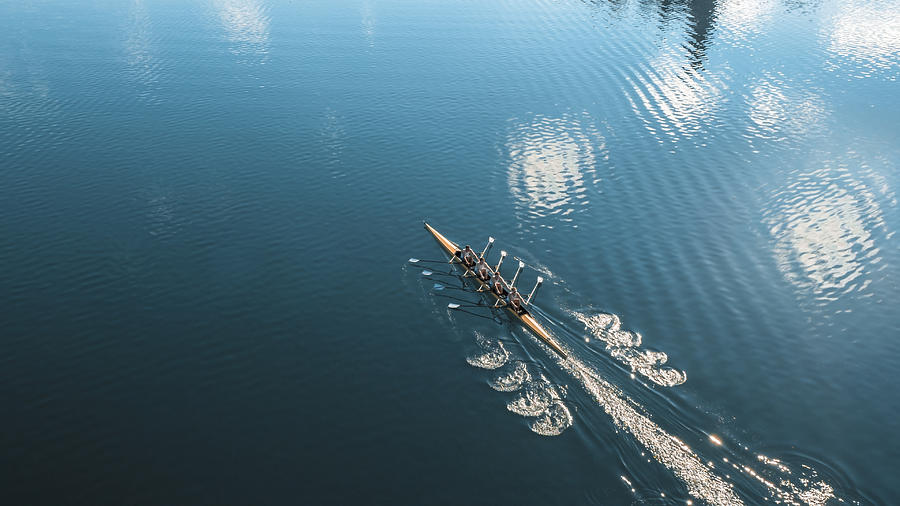 Four male athletes sculling on lake in sunshine #1 Photograph by Simonkr