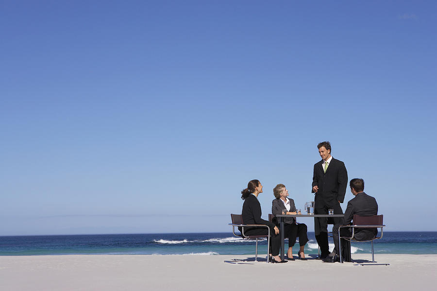 Four Well-Dressed Businessmen and Businesswomen Sit at a Table on a Beach, Having a Meeting #1 Photograph by Digital Vision.