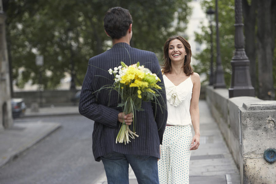 France, Paris, young couple outdoors, man holding flowers behind back #1 Photograph by Rayes