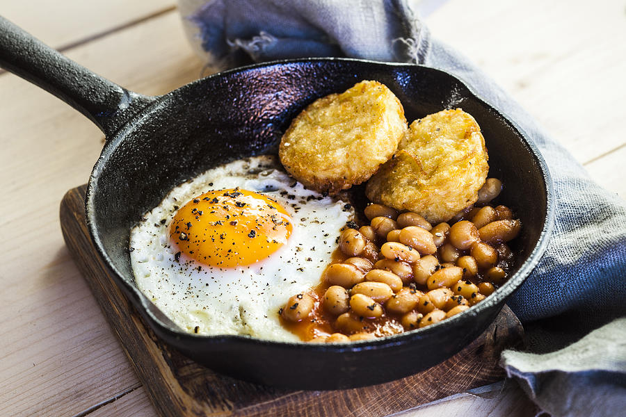 Fried egg, baked beans and hash browns in frying pan on wooden board #1 Photograph by Westend61