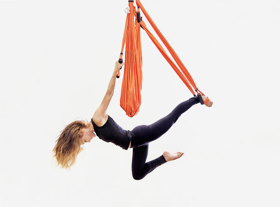 Front view of blonde woman hanging on orange swing practicing aerial yoga. #1 Photograph by Ruben Bonilla Gonzalo