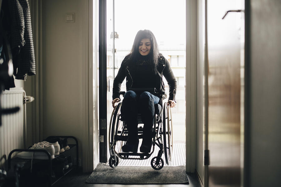 Full length of smiling young disabled woman entering home #1 Photograph by Maskot