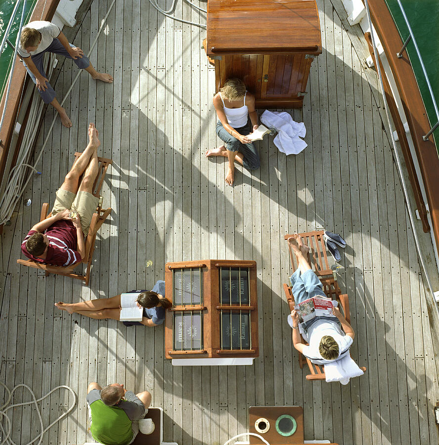 Group of friends reading on deck of sailboat, overhead view #1 Photograph by Mike Powell