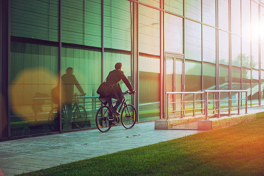 Handsome man riding bicycle beside the modern office building #1 Photograph by Gruizza