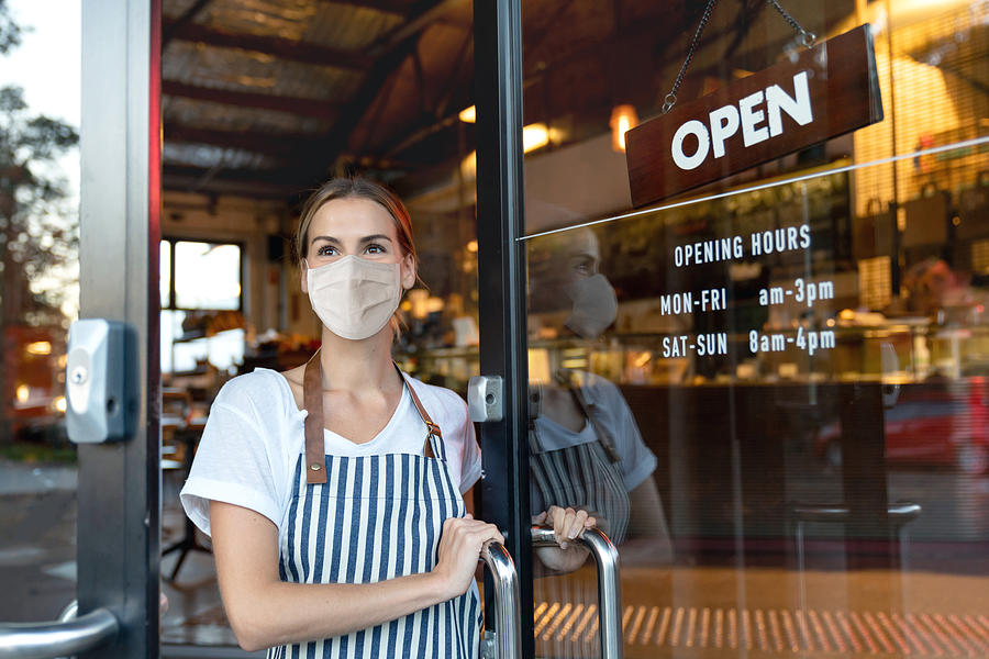 Happy business owner opening the door at a cafe wearing a facemask #1 Photograph by Andresr
