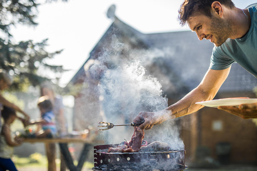 Happy man grilling meat on a barbecue grill outdoors. #1 Photograph by Skynesher
