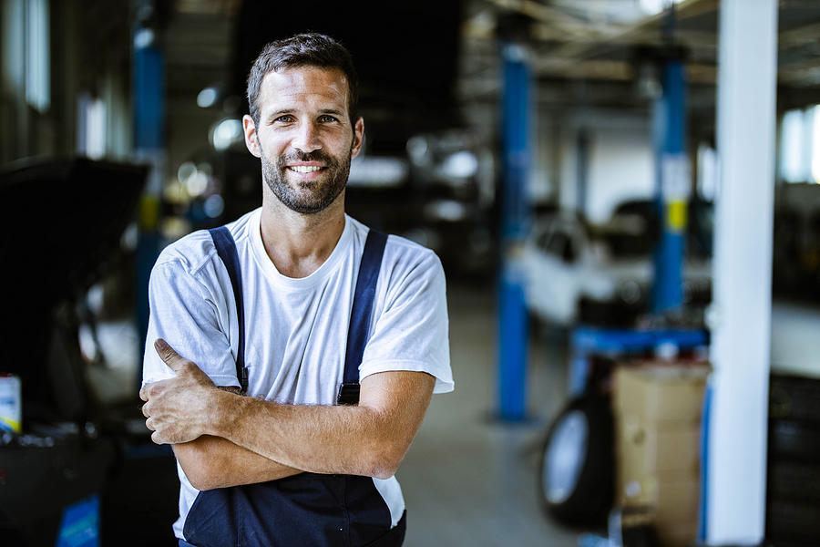 Happy mechanic with crossed arms in auto repair shop. #1 Photograph by Skynesher
