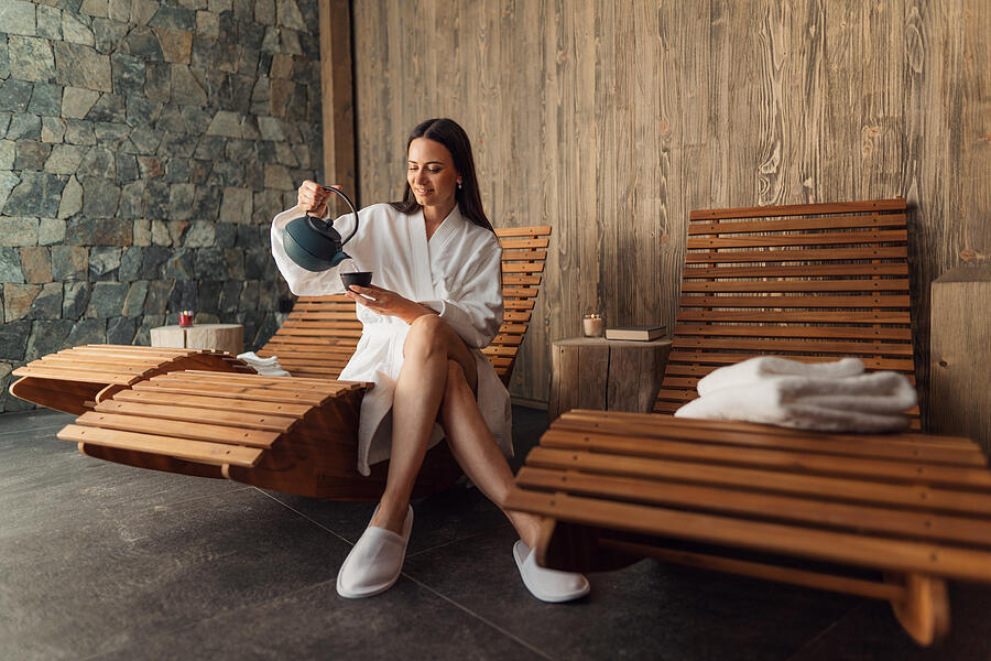 Happy mid adult woman with bathrobe sitting in wellness resort, relaxing. #1 Photograph by Halfpoint Images