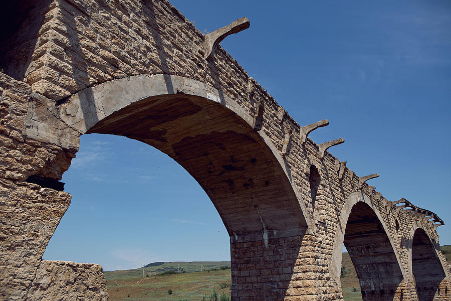 high ruined stone bridge stands in the summer in a field above the ...