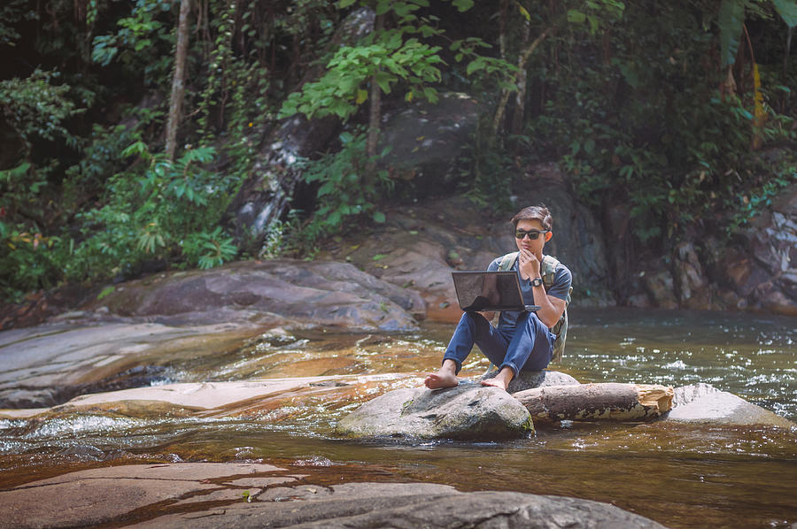Hiker with backpack and laptop and phone at  waterfall  the forest. #1 Photograph by Primeimages