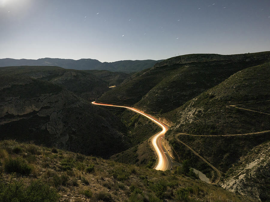 Lights and trails of vehicles circulating along a road of mountain with curves closed in the night. Valencian Community, Spain #1 Photograph by Jose A. Bernat Bacete