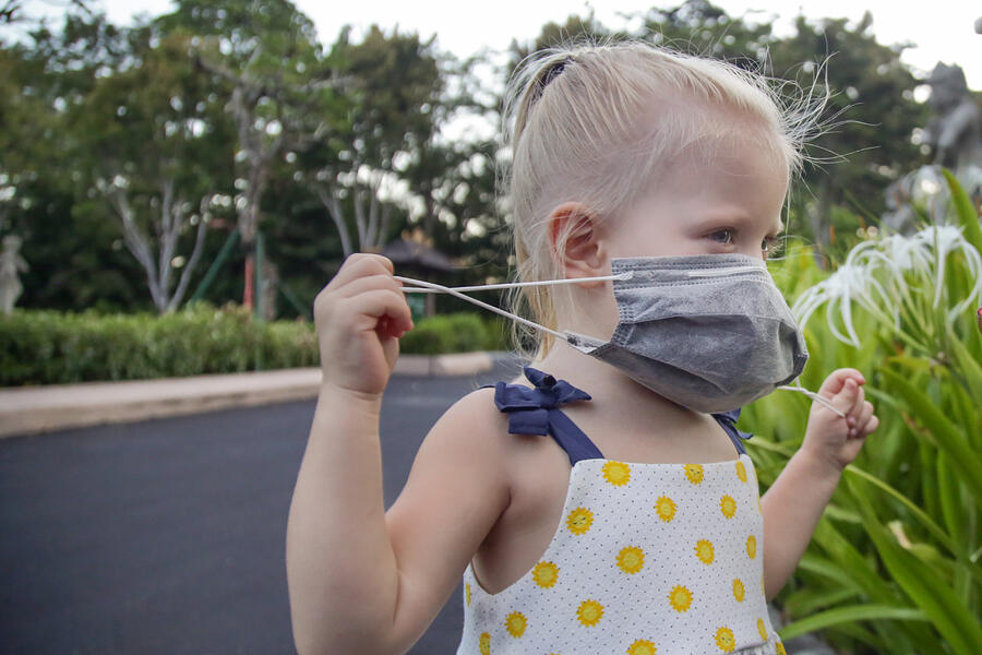 Little toddler girl trying to put medical protective mask. Candid outdoor portrait of child with medical mask. Corona virus outbreak or air pollution concept. #1 Photograph by Triocean