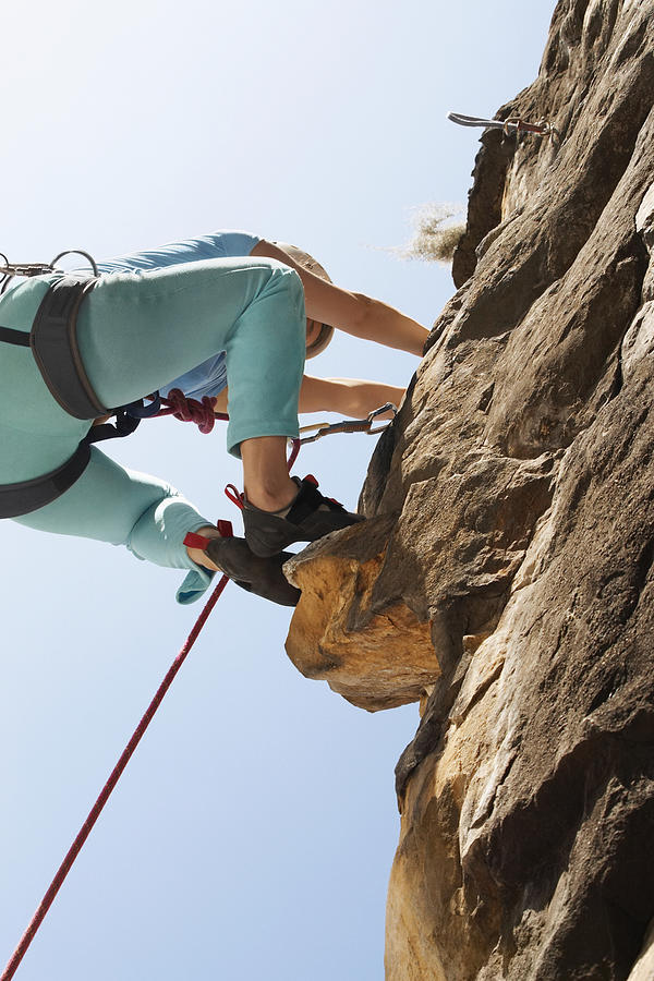 Low angle view of a female rock climber scaling a rock face #1 Photograph by Glowimages