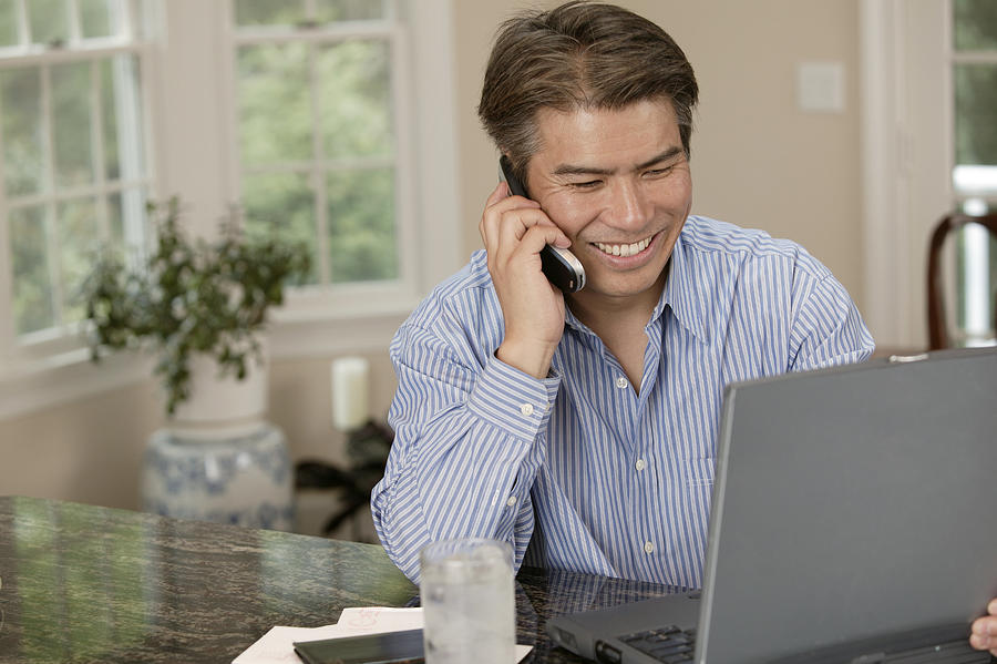 Man using laptop and talking on cell phone #1 Photograph by Comstock Images