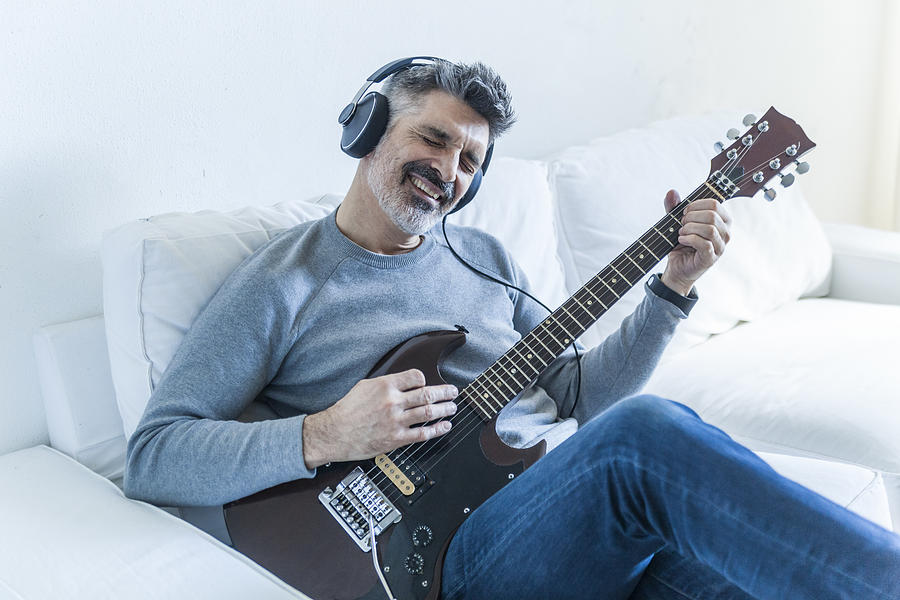 Mature man at home playing electric guitar and wearing headphones #1 Photograph by Westend61