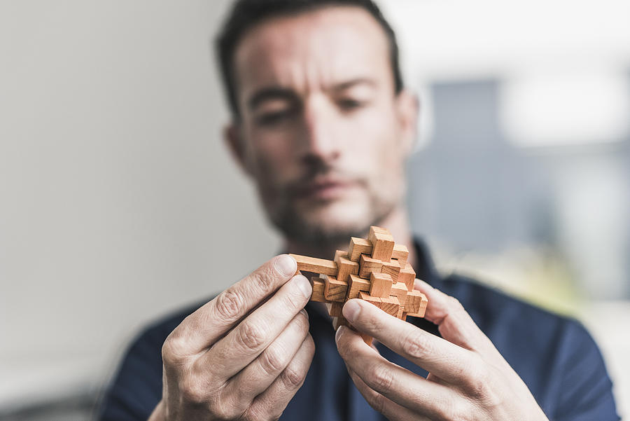 Mature man sitting in office assembling wooden cube puzzle #1 Photograph by Westend61