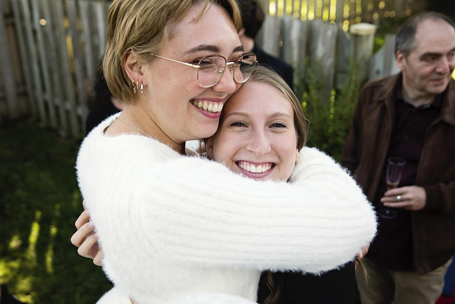 Millennial bride hugging sister at wedding cocktail in backyard. #1 Photograph by Martinedoucet