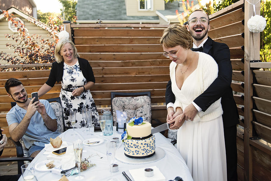 Millennial newlywed couple cutting cake at wedding cocktail in backyard. #1 Photograph by Martinedoucet