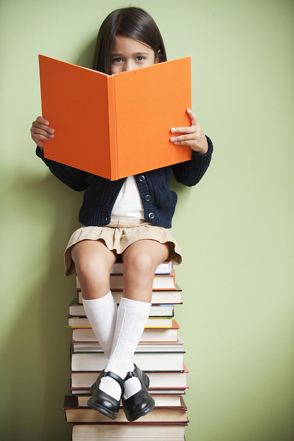Mixed race girl sitting on stack of books reading book #1 Photograph by Jose Luis Pelaez Inc
