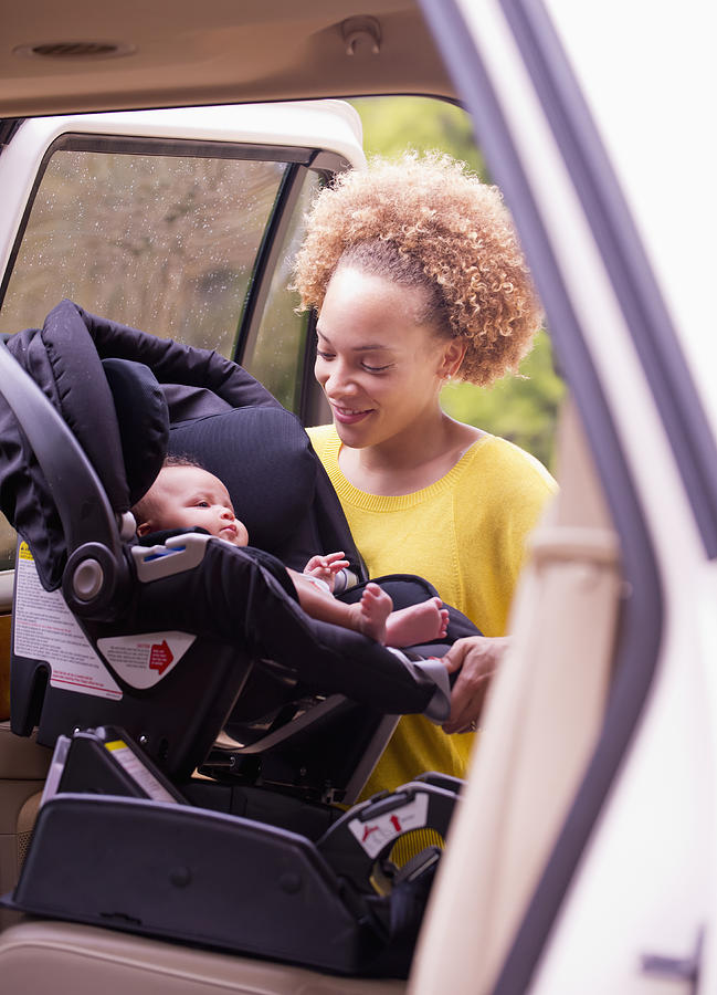 Mixed race mother loading baby into car seat #1 Photograph by Ariel Skelley