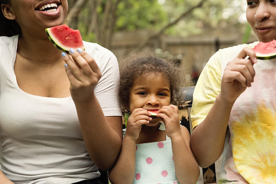 Mixed-race sisters eating watermelon in backyard. #1 Photograph by Martinedoucet